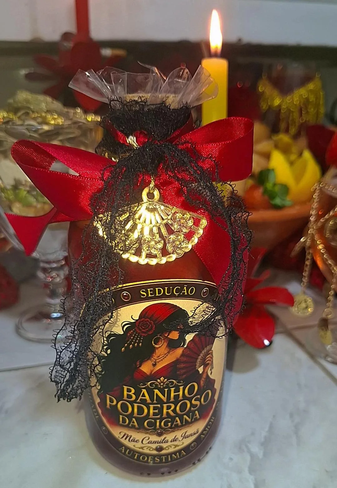 Frasco do Banho Poderoso da Cigana decorado com fitas vermelhas, renda preta e pingente dourado