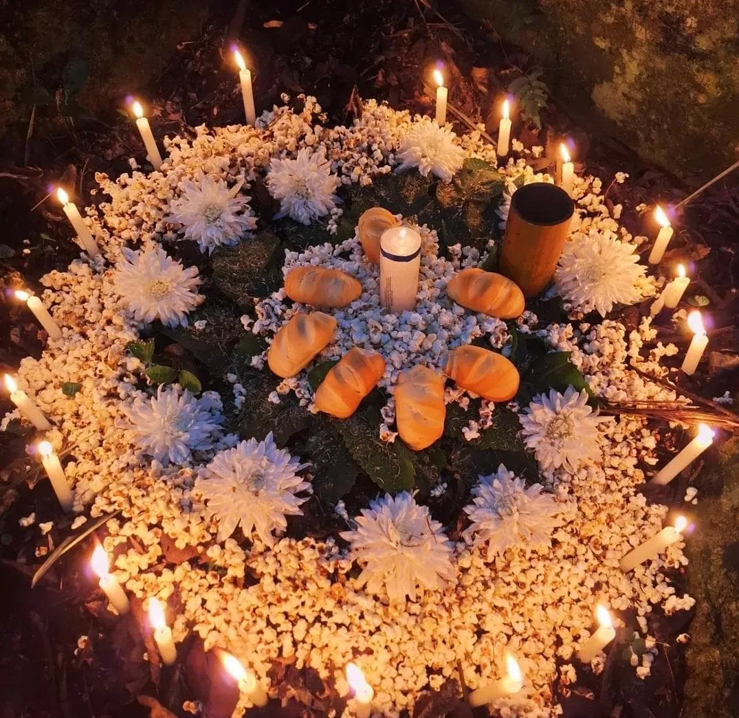 Oferenda circular ao ar livre com flores brancas, pães e muitas velas acesas
