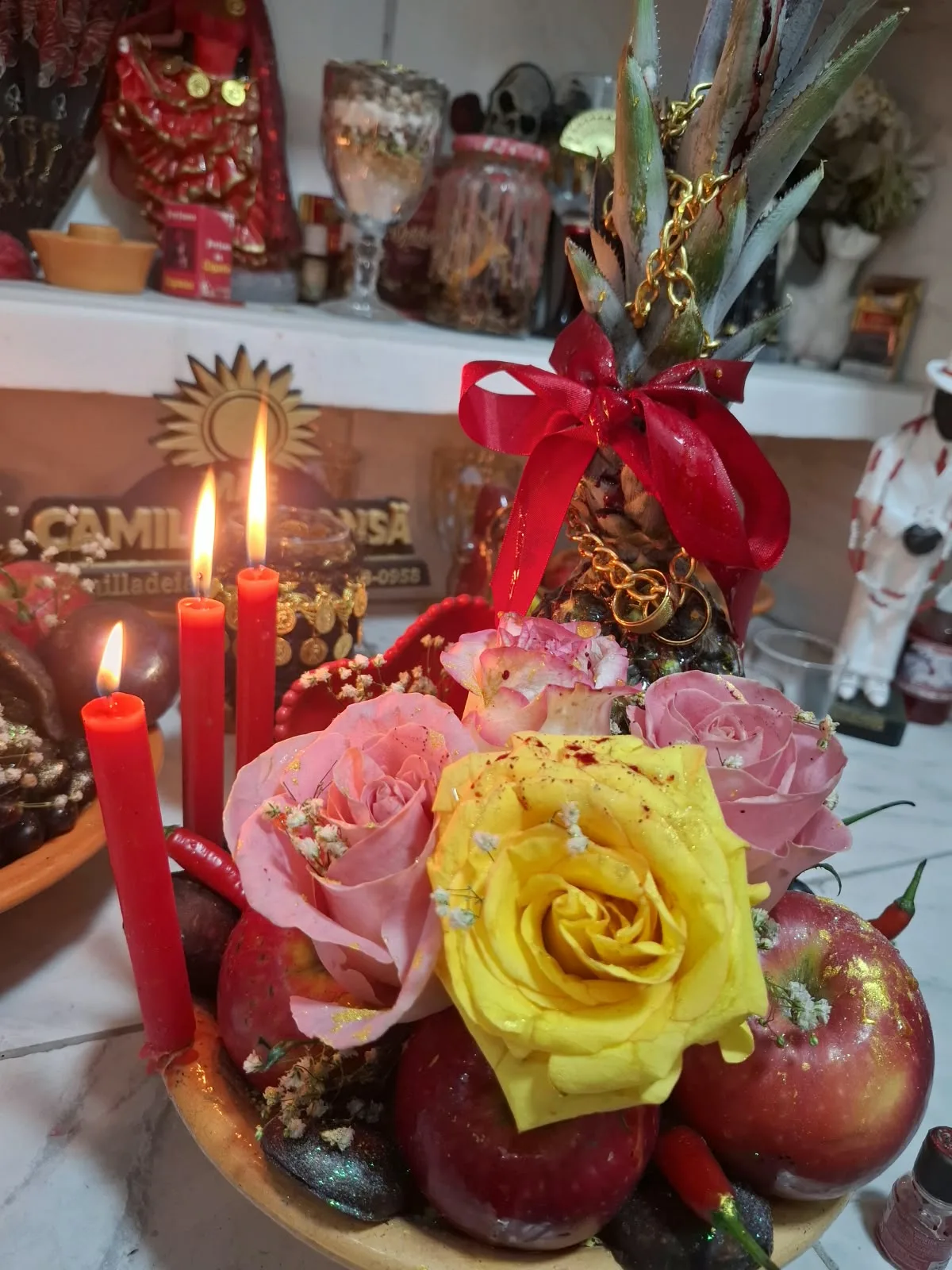 Arranjo espiritual com abacaxi, maçãs, rosas e velas vermelhas