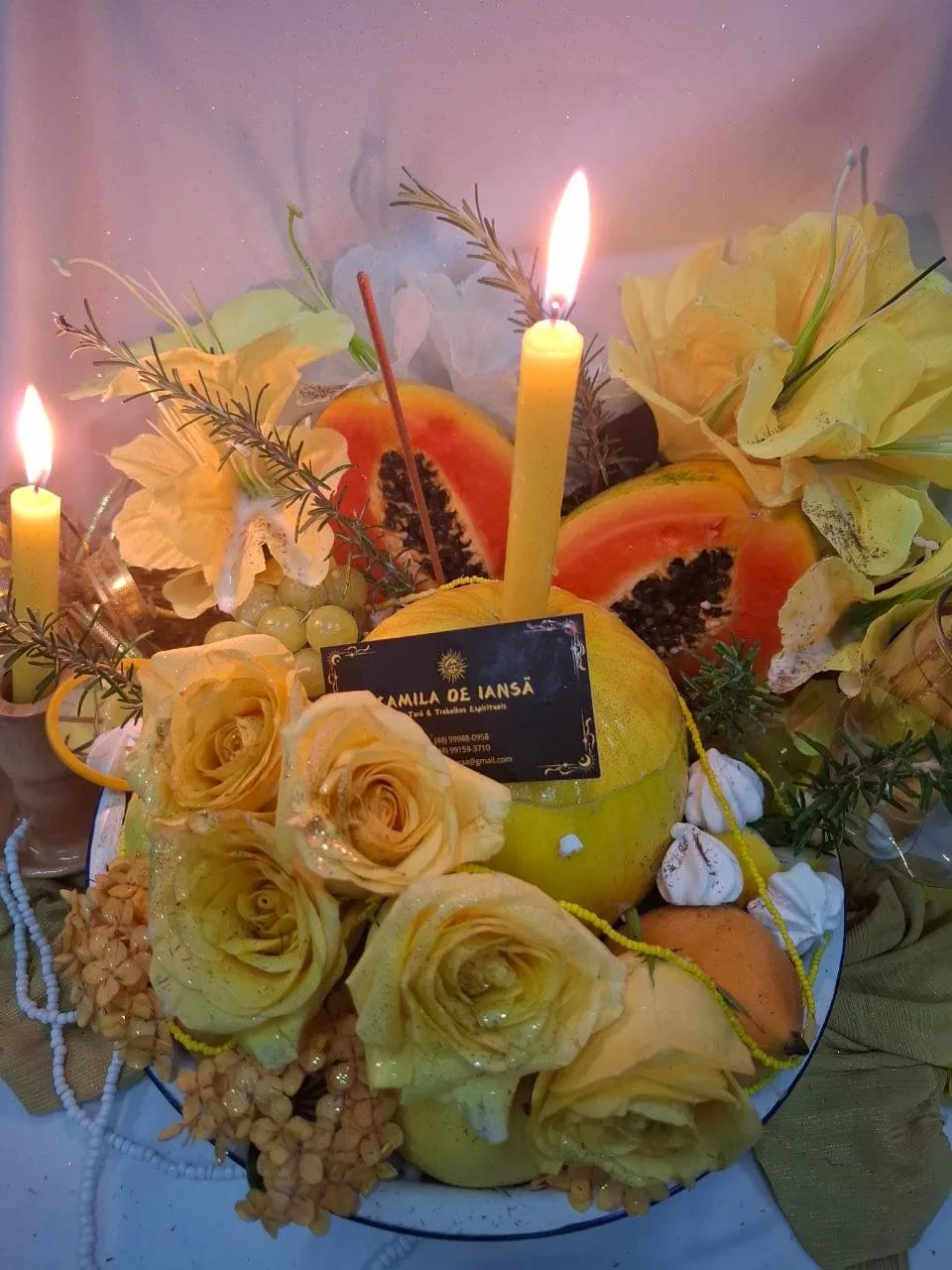 Trabalho em tons amarelos com rosas, mamão, uvas, grãos e velas acesas