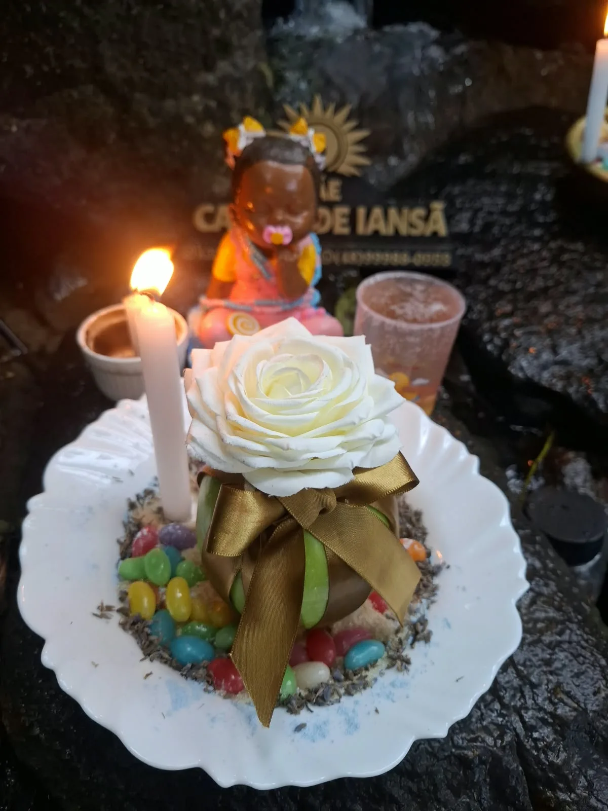 Rosa branca com laço dourado sobre um prato, ao lado de vela acesa