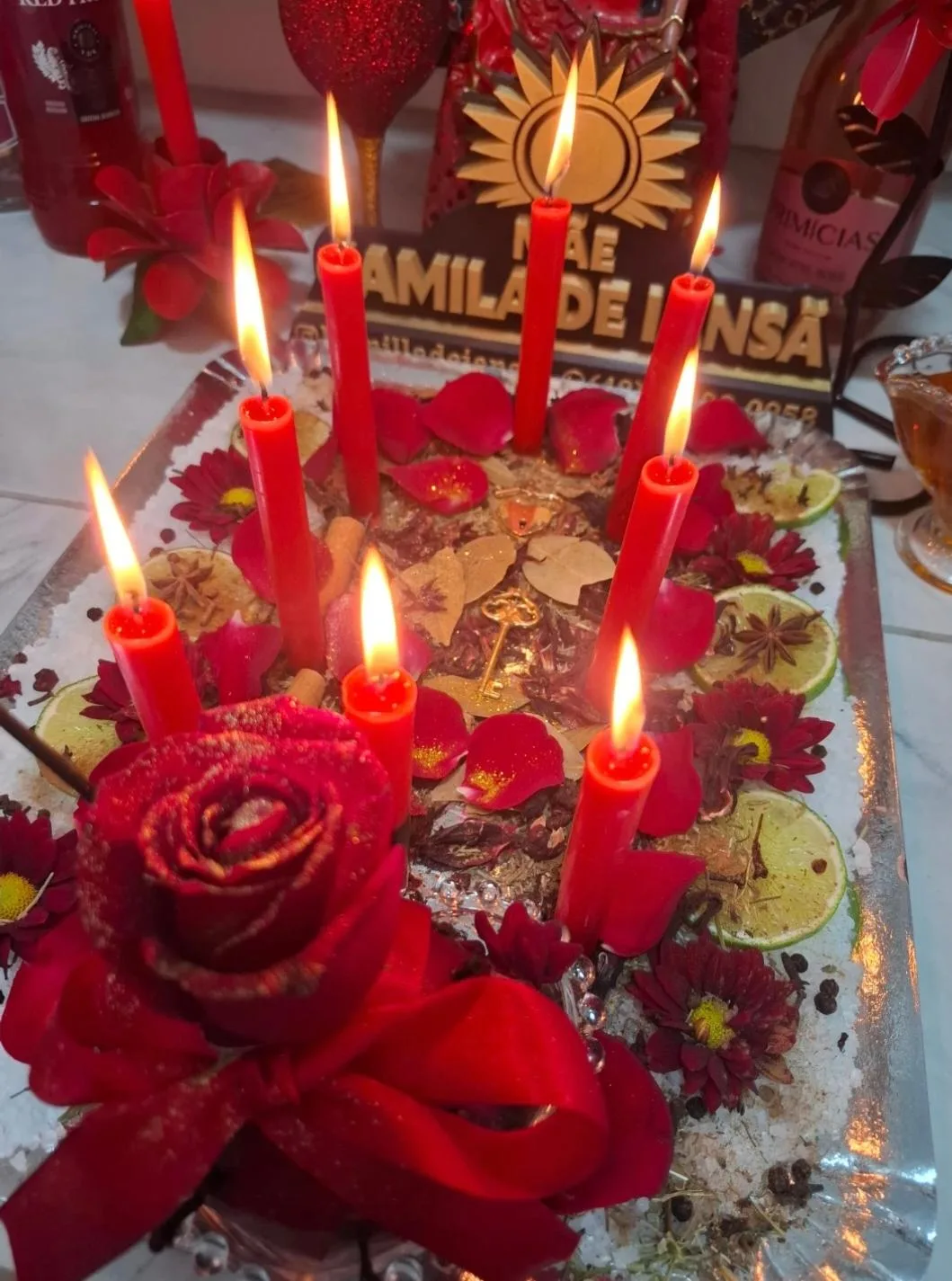 Sete velas vermelhas acesas entre flores, ervas, pétalas e especiarias