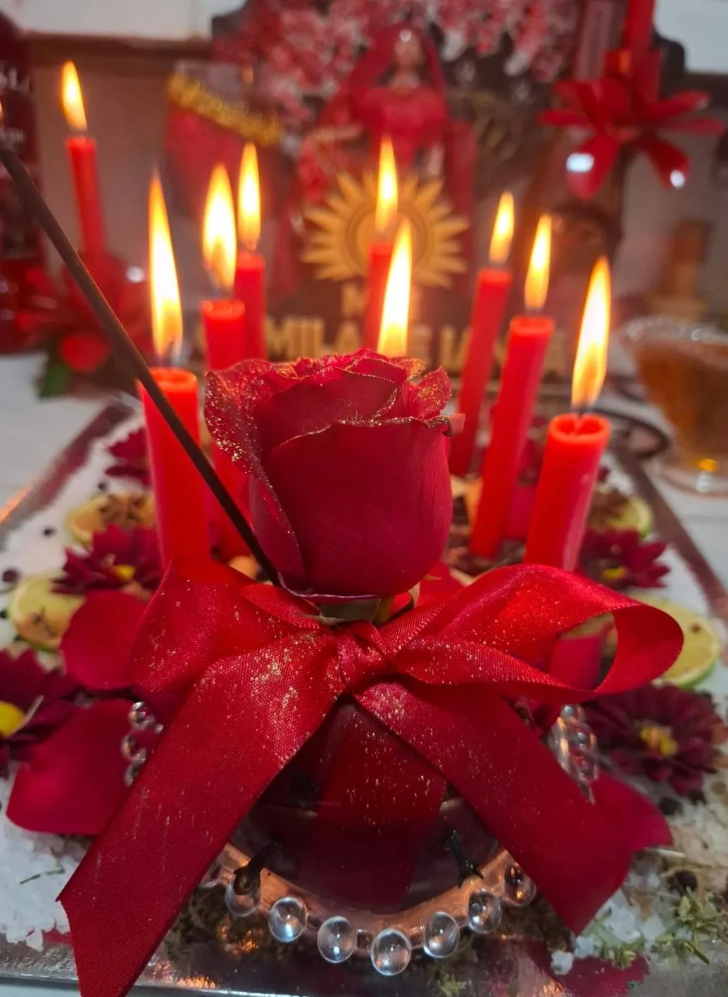 Rosa vermelha envolvida por laço diante de velas vermelhas acesas
